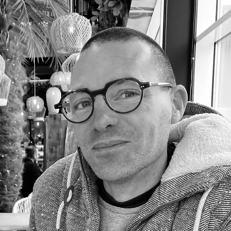 Homme portant des lunettes rondes, en gros plan, devant un décor flou