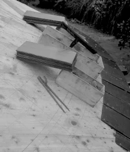 Composition d'outils manuels de couverture : marteau, enclume, compas, posés sur un support en bois.